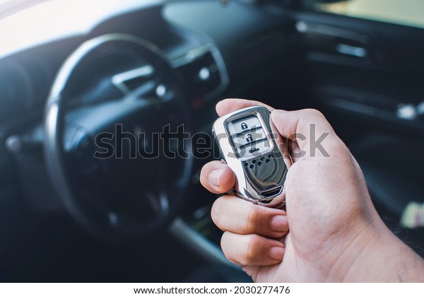 Car keyless entry remote in a hand of\
the owner car with car interior blurred\
background