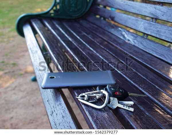 Car keys and mobile phones on the park bench Loss\
of property due to forgetting On the background of a black wooden\
bench With copy space.