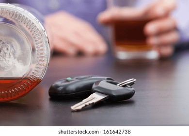 Car keys sittuated near the almost empty bottle of alcohol and the hands holding a filled glass
