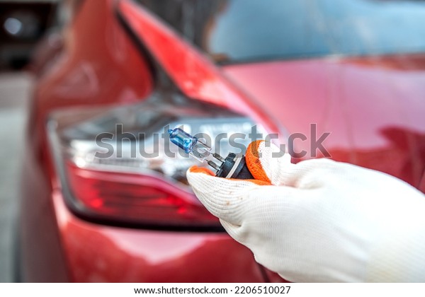 car lamp in a hand on\
the background of a car headlight. Car repair. a car mechanic\
changes a light bulb.