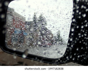 Car Left Side Mirror In The Heavy Rain. Lots Of Rain Droplets Everywhere. An American Town Main Street Silhouette Can Be Guessed In The Reflection. No People Or Trademarks.