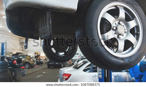 Car lifted in automobile service for fixing,\
worker repairs detail