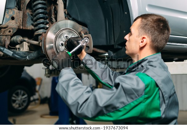 Car lifted in automobile service for fixing, worker\
repairs the wheel