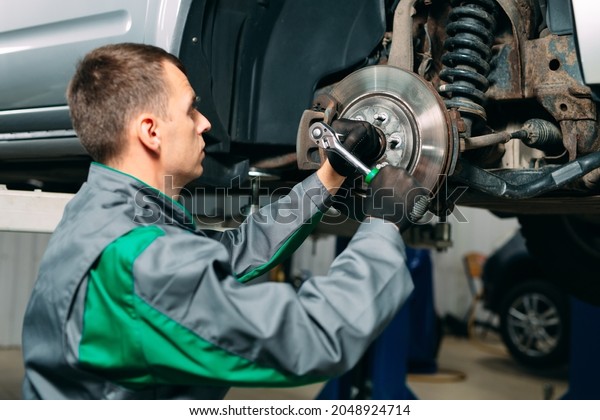 Car lifted in automobile service for fixing, worker\
repairs the wheel