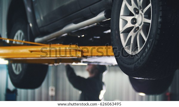 Car lifted in automobile service for fixing,\
worker repairs detail