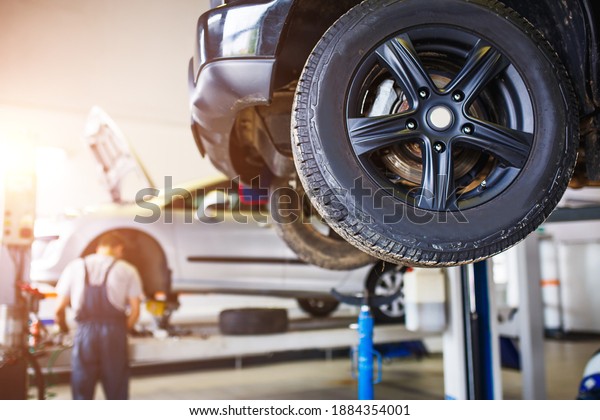 The car is lifted for repair on a lift in a\
car service station, a mechanic in overalls repairs in the\
background. Wheel close-up, tire\
service