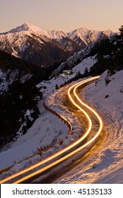 Car Light In Night On Ice Road In Snow Winter Mountain.