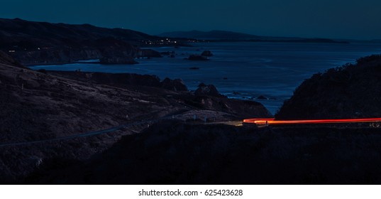 Car Light Trail On A Windy Road Near A Beach Town At Night