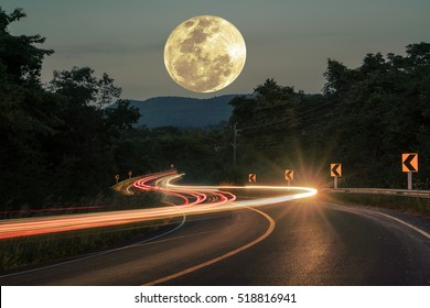 Car Light Trail Sparkly On Long Macadamized S-curvy Road With Trees And Beautiful Full Moon Sky At Night Time: Countryside Thailand
