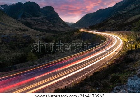Car light trails on winding road through the highlands near Glencoe in Scotland at dusk - Travel and transport concepts in a scenic place with beautiful nature and views