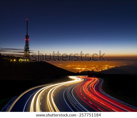 car lights at night towards the city and communications antenna
