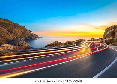 car lights on road landscape photographed with long exposure technique at the colorful sunset on the beach. drive on the coast freeway of spain. Light of car driving on sea coastal highway in summer. - Powered by Shutterstock