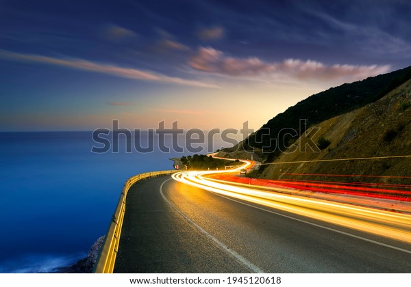 Car lights on\
the sea and highway. Car lights on the coastal road show the speed\
in traffic. Fast car lights on the road passing by the beach at\
sunset. Mudanya, Bursa,\
Turkey.