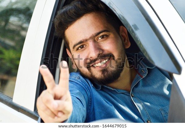 car loan concept, happy indian man showing victory\
sign from car window