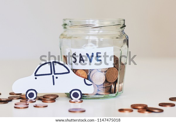Car loan, car insurance concept.\
Glass jar full of coins and paper car on white\
background