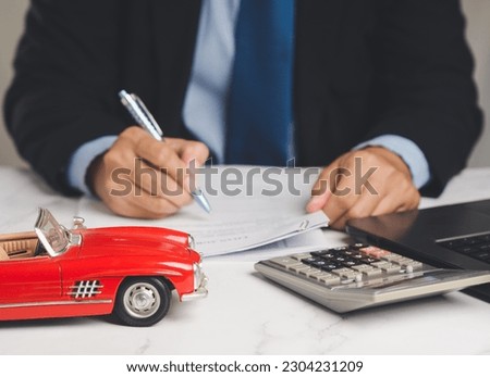 Car loan or Title loan. A Businessman signs a contract loan agreement while sitting at the table. Miniature a red car model, a calculator, and a laptop on a table. Car finance and insurance concept