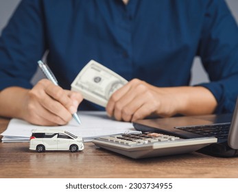 Car loan or Title loan. US dollar bills in a hand businessman while sitting at the table. Miniature a red car model, a calculator, and a laptop on a table. Car finance and insurance concept