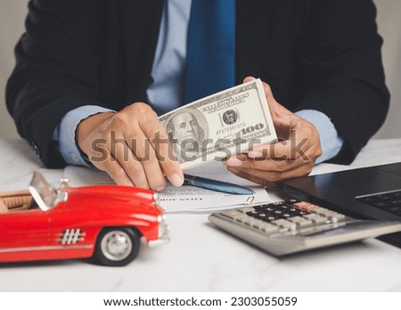 Car loan or Title loan. US dollar bills in a hand businessman while sitting at the table. Miniature a red car model, a calculator, and a laptop on a table. Car finance and insurance concept