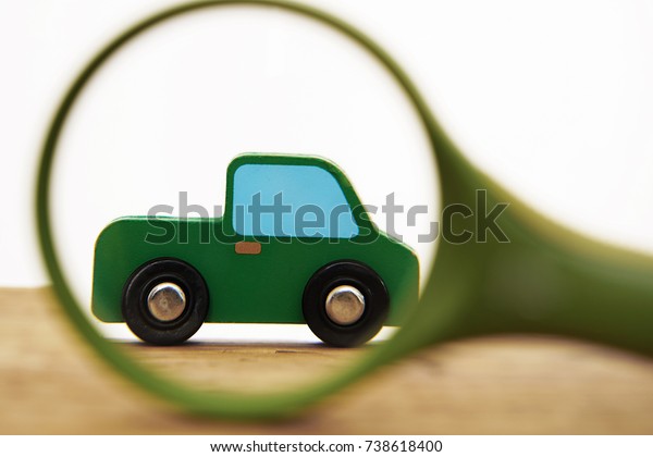 car with magnifying glass - car reviewer -\
isolated on white background. wooden table. searching green car.\
Magnifying glass with green car. Search testing service of the\
automobile