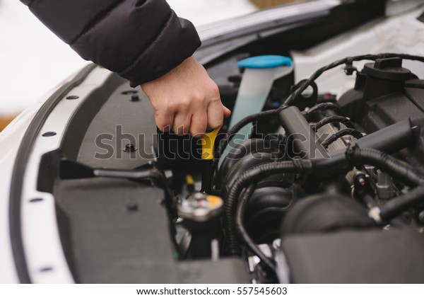 Car maintenance\
before winter. Man checking oil level in his car using dipstick.\
Outdoor closeup photograph