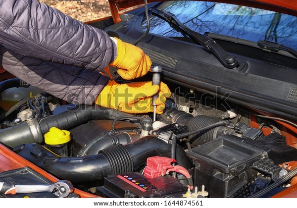 Car maintenance and repair\
concept. Hands of driver in orange rubber gloves checks car using\
tools, open hood. Automobile and transportation, close\
up.