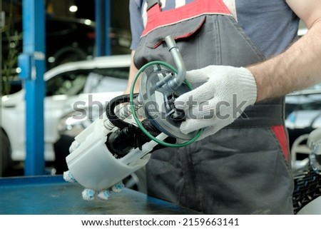 Car maintenance at a car service. An auto mechanic holds a new fuel pump in his hands. Repair of the fuel and exhaust system of the car.