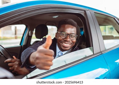 Car. Man Driver Happy Smiling Showing Thumbs Up Coming Out Of Blue Car Side Window On Outside Parking Lot Background. Young Man Happy With His New Vehicle. Positive Face Expression