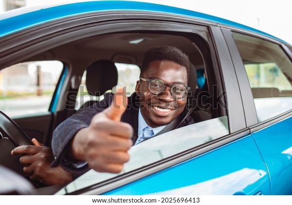Car. Man driver\
happy smiling showing thumbs up coming out of blue car side window\
on outside parking lot background. Young man happy with his new\
vehicle. Positive face\
expression