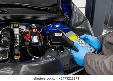 Car master mechanic checking and testing automotive battery with digital electronic battery tester and analyzer in auto vehicle workshop. - Powered by Shutterstock