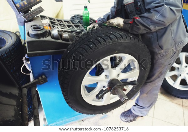 Car mechanic balancing car wheel on\
computer machine balancer in auto repair service,\
toned