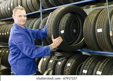 Car Mechanic In Blue Overalls Pulls A Tire From The Tire Store In The Garage