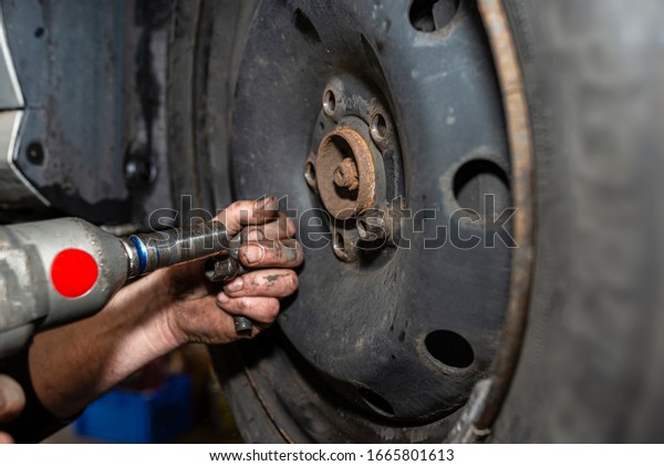 The car mechanic bolts\
the steel car wheel with a pneumatic wrench in a car workshop,\
visible male hands.