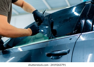 a car mechanic carefully sticks a protective tinted film on a car glass at detailing station - Powered by Shutterstock