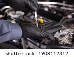the car mechanic carries out diagnostics and replacement of a car spark plug in the engine. holds a new auto part. black mittens
