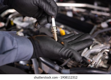 The Car Mechanic Carries Out Diagnostics And Replacement Of A Car Spark Plug In The Engine. Holds A New Auto Part. Black Mittens
