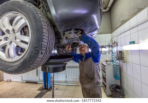 Car\
mechanic changes oil in a workshop. Mechanic standing under the car\
and draining oil into a special cannister via\
funnel.