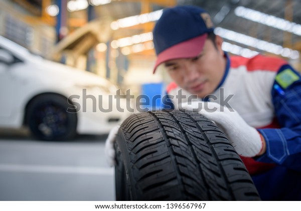 A car mechanic or mechanic changes a young tire\
in a uniform, checking the new tires while working in the car\
service.