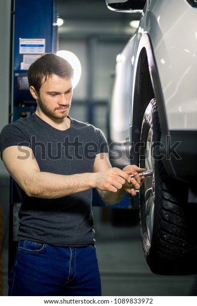 Car mechanic changing tire with manual tool in\
epair garage