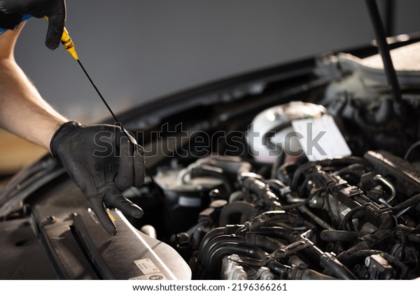 The car mechanic is checking the engine oil level.\
Overheating of car engine. Motor with open hood. Checking the\
engine oil car maintenance Remove the dipstick to view the engine\
oil level.