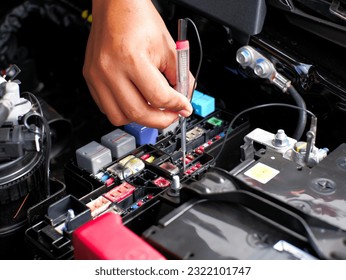 car mechanic checking the fuse connection using a multimeter and a test pen in the car fusebox - Shutterstock ID 2322101747