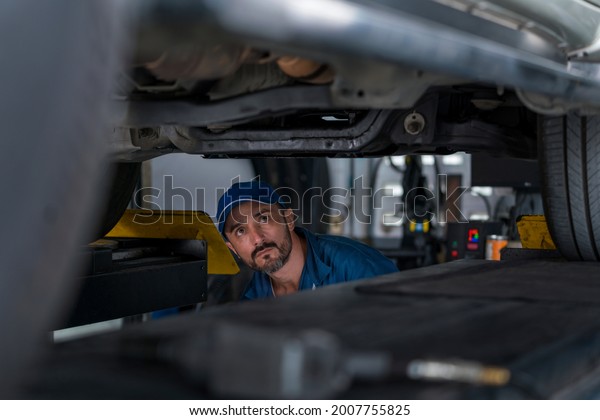 Car mechanic checking the car\
suspension. Mechanic man or smith repairing car at\
garage.