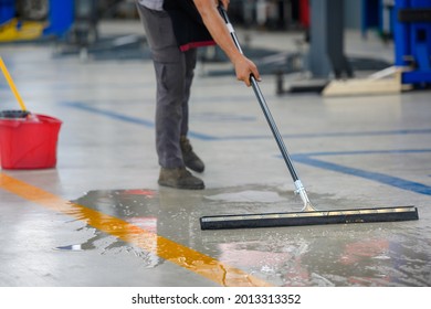 Car Mechanic Cleaning The Garage Floor At The Auto Industry Shop Workshop Use A Mop To Clean Water From The Epoxy Floor In The Car Repair Center.