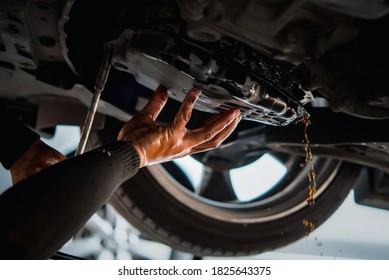 Automechaniker entwässern die alte automatische Getriebeflüssigkeit (ATF) oder Getriebeöl in der Automobil-Werkstatt zum Umstellen des Öls in einer Getriebeschachtel