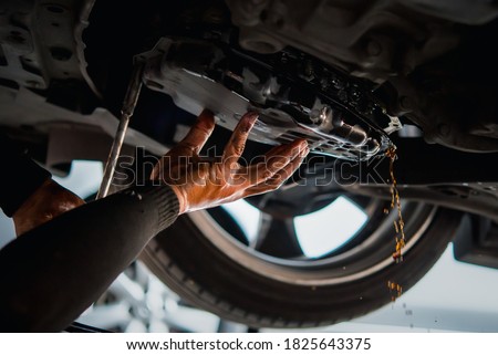 Car mechanic drain the old automatic transmission fluid (ATF) or gear oil at car garage for changing the oil in a gear box of car engine