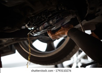 Car mechanic drains the old automatic transmission fluid (ATF) or gear oil at car garage for changing the oil in a gear box of car engine