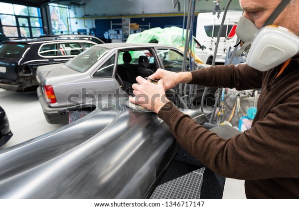 Car mechanic with dust mask\
grinds a car part in a service station - Serie car repair\
workshop