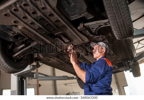 Car mechanic examining lifted car at repair service
station. Using tools