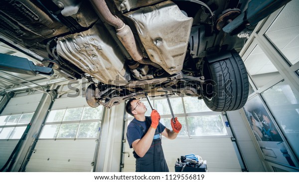 Car mechanic examining car\
suspension of lifted automobile at repair service station.\
Background