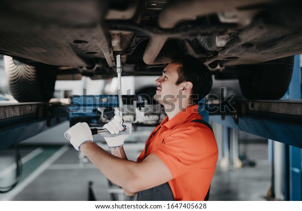 car mechanic examining car suspension of
lifted automobile at repair service
station