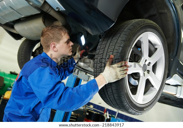 car mechanic examining car suspension of\
lifted automobile at repair service\
station